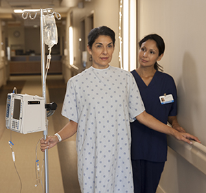 Paciente mujer que camina por el pasillo de un hospital con un soporte IV junto a una enfermera.