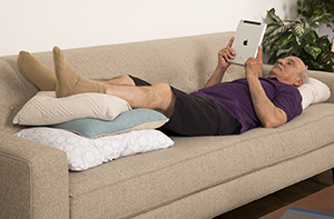 Hombre recostado en un sofá, con las piernas apoyadas sobre almohadas.